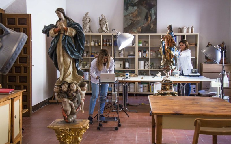Taller de restauración de la Abadía del Sacromonte, en donde dos mujeres están restaurando las esculturas de unas Virgenes.
